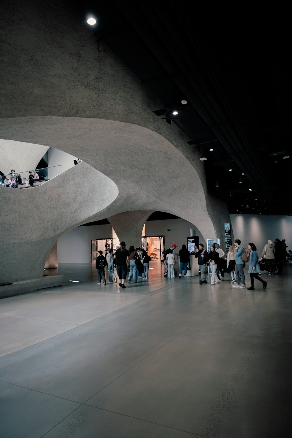 Persone esplorano un moderno museo in cemento con soppalchi.